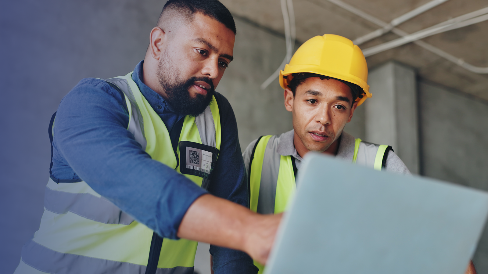 Two construction workers, on a job site, looking at a laptop
